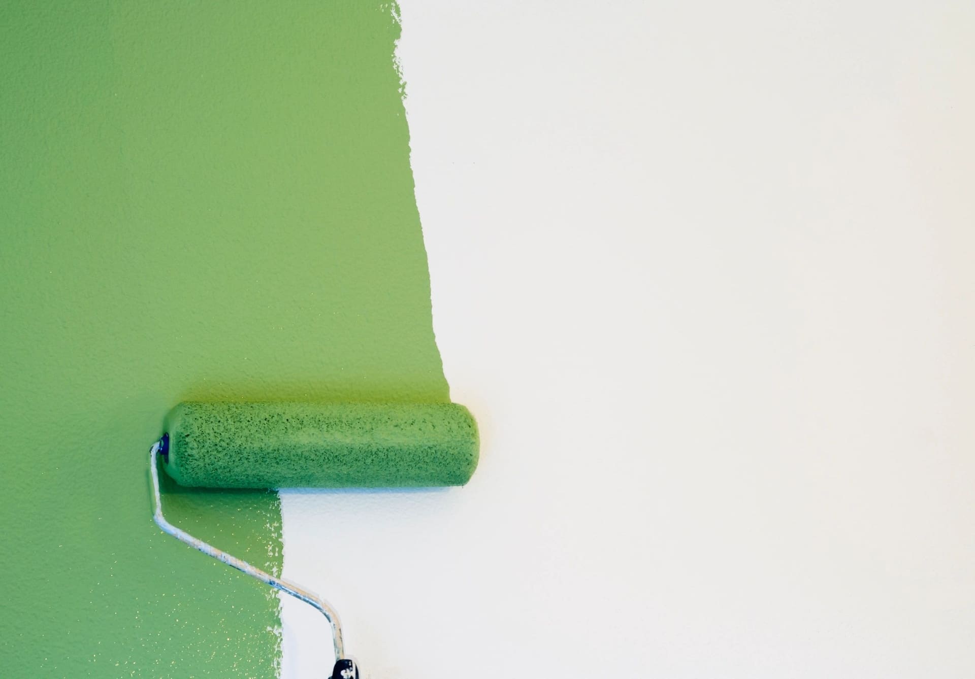 A paint roller applying green paint to a white wall