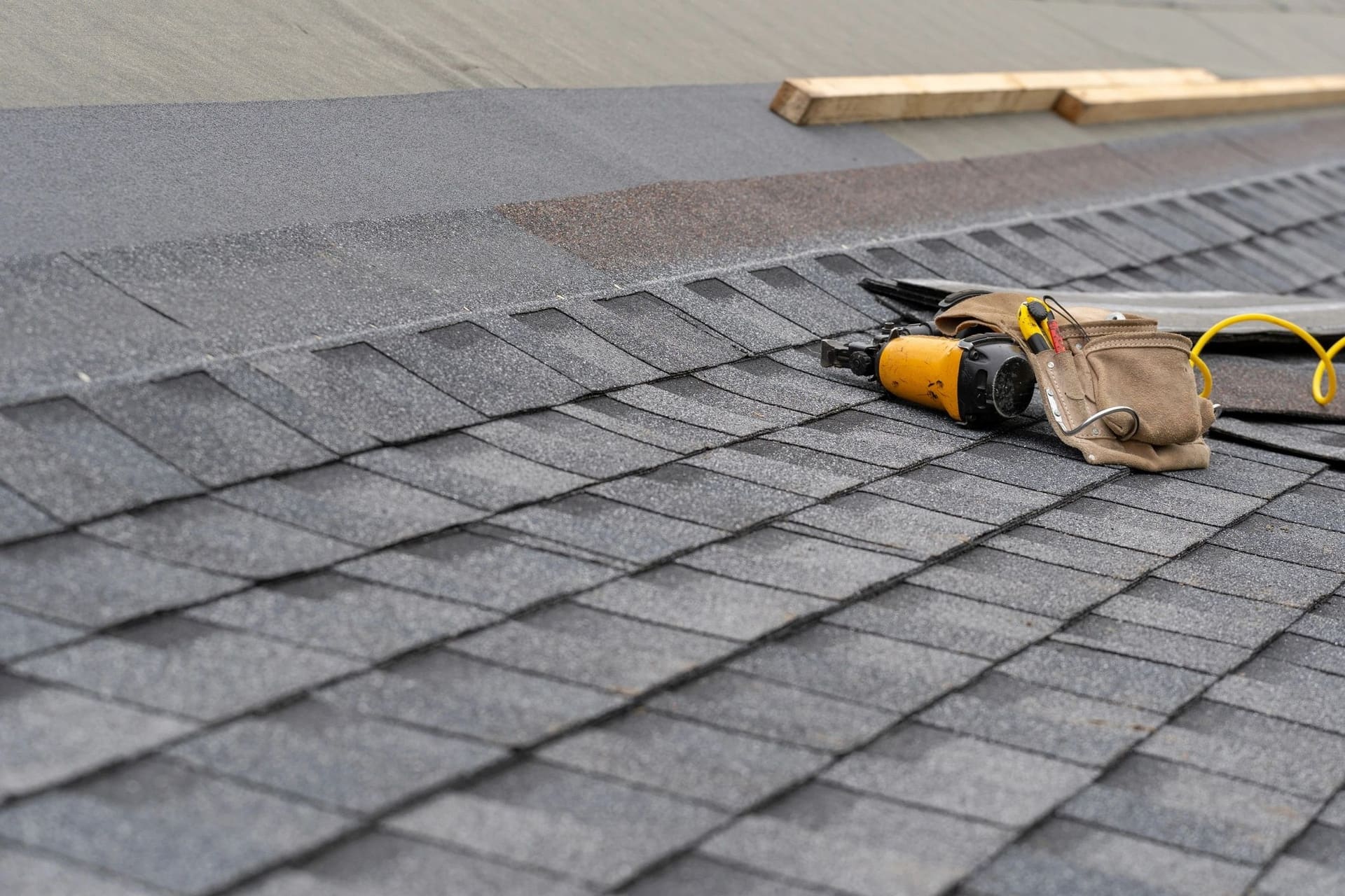 Asphalt roof shingles with a tool belt and nail gun during a roof repair