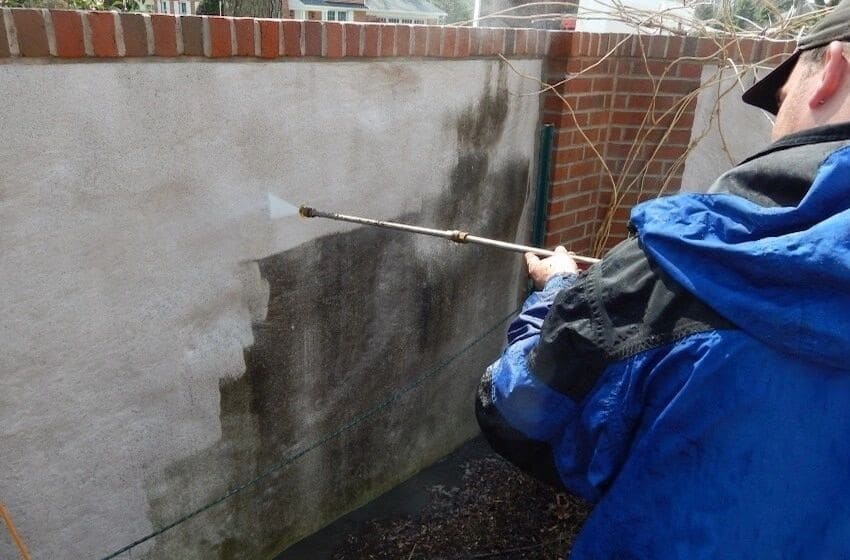 An ASJ technician pressure washing algae off a stucco wall