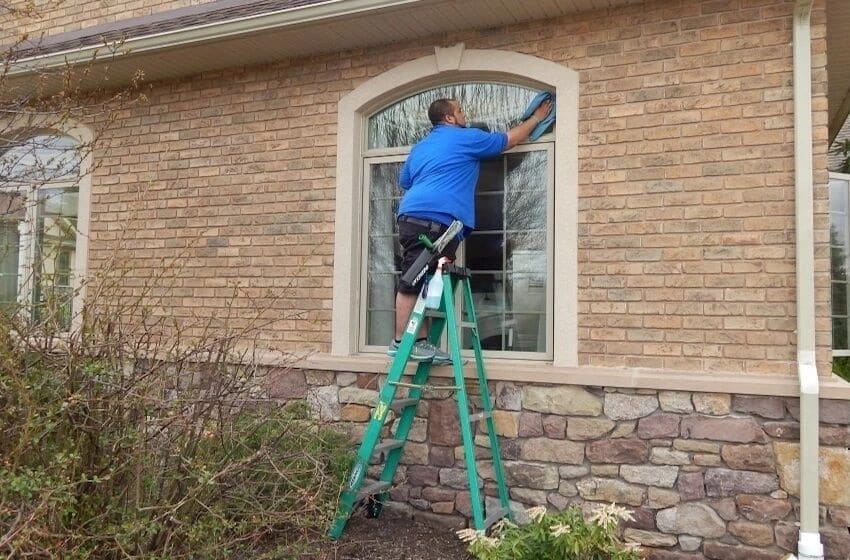 An ASJ technician on a ladder cleaning an arched window on a brick and stone house